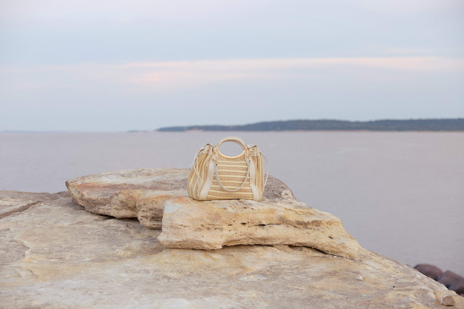 Bolsa de palha bege com alça circular em pedra à beira-mar, design brasileiro e sofisticado