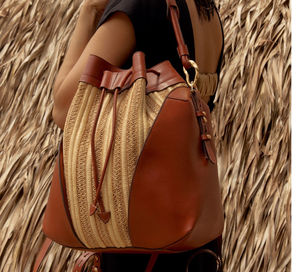 Bolsa bucket em couro marrom e palha com detalhes dourados, ideal para looks casuais e sofisticados.