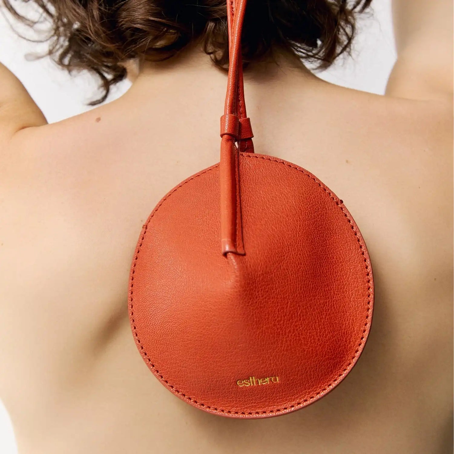 Bolsa circular em couro laranja com design minimalista e detalhe da marca esthera