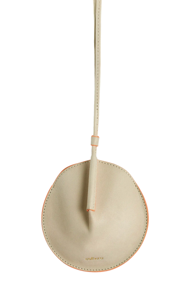 Bolsa circular em couro bege com detalhe laranja e alça fina, design minimalista e sofisticado.