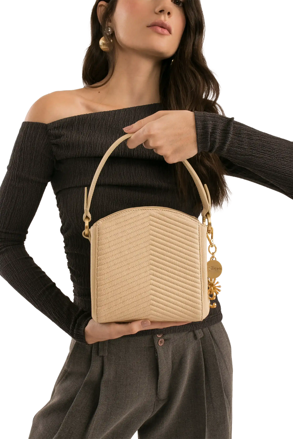 Bolsa bege com textura em V, alça de mão e detalhes dourados, combinando com look elegante.