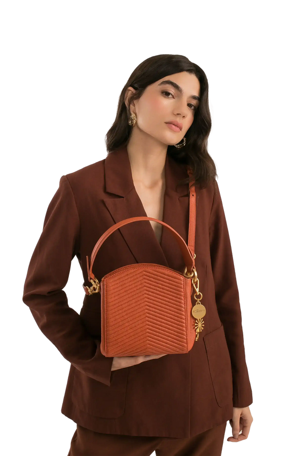 Bolsa feminina em tom terroso com costura em V, alça de mão e detalhes dourados, combinando com blazer marrom.