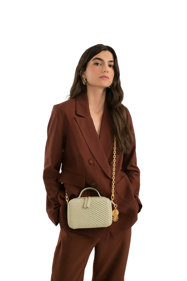 Bolsa pequena com alça de corrente dourada e design acolchoado, combinando com terno marrom