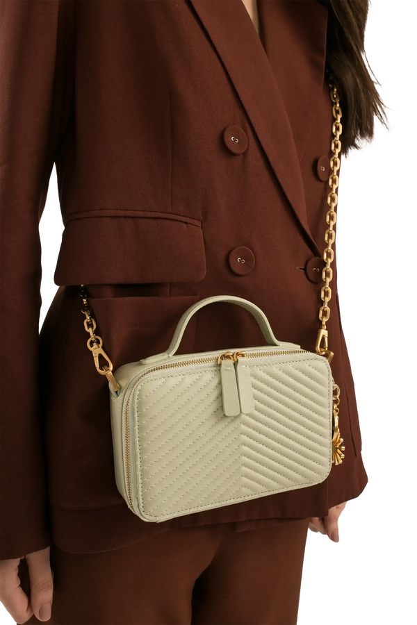 Bolsa verde claro com alça de corrente dourada e costura em V, combinando com blazer marrom