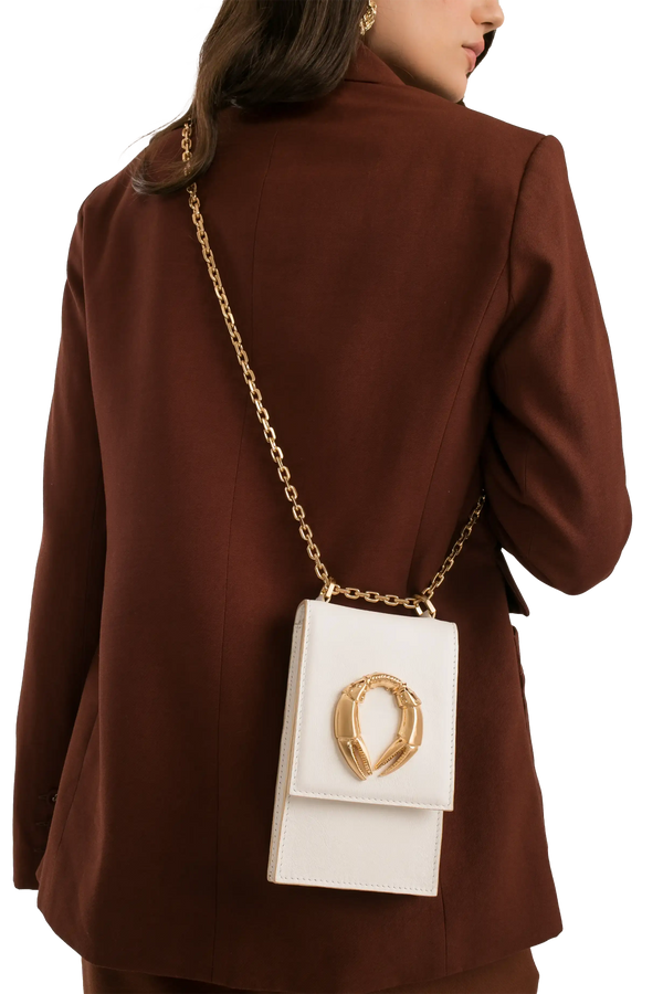 Bolsa branca com corrente dourada e detalhe metálico, usada com blazer marrom. Acessório elegante e sofisticado.