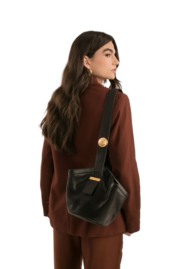 Bolsa preta com detalhe dourado, usada por mulher em look marrom, estilo sofisticado e funcional