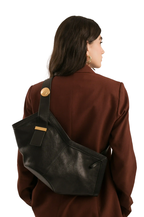 Bolsa preta de couro com detalhes dourados, usada por mulher com blazer marrom