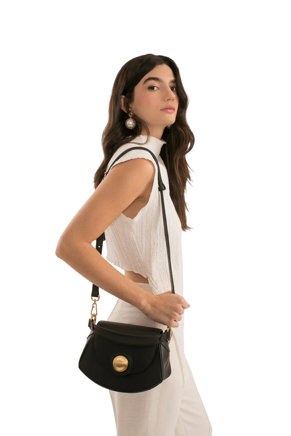 Bolsa preta com detalhe dourado, usada por modelo em look branco, estilo sofisticado e funcional