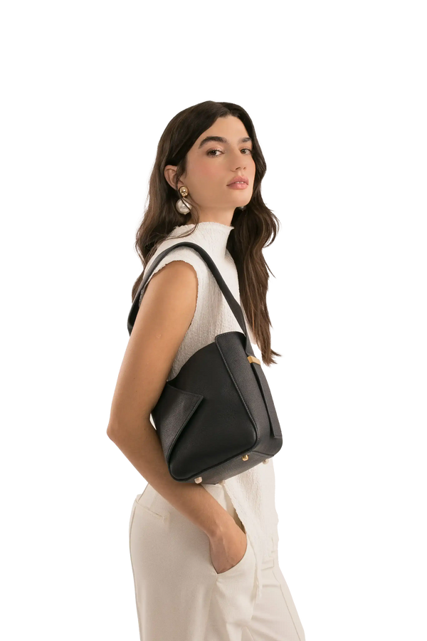 Bolsa preta de ombro com design moderno e detalhes dourados, usada com look branco elegante.