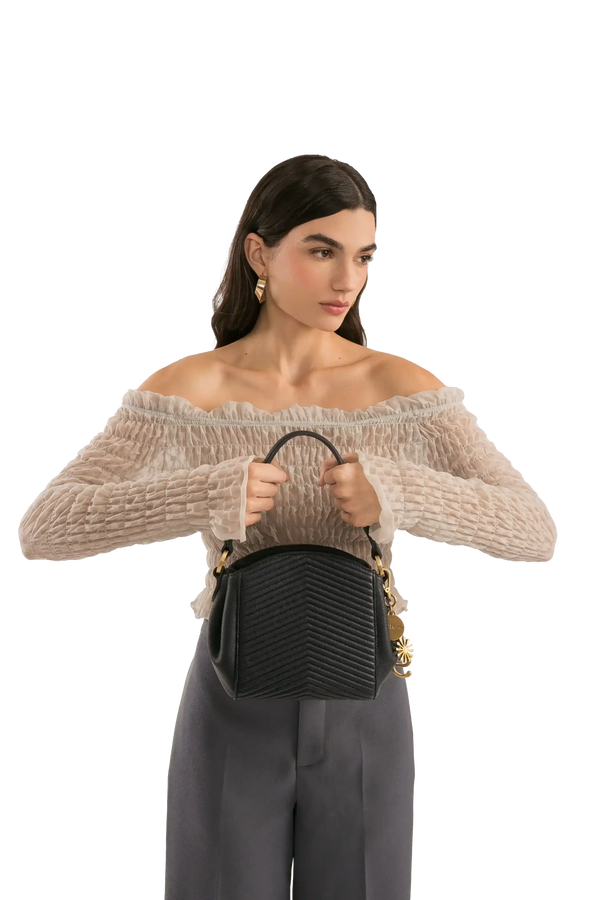 Bolsa preta texturizada com alça e detalhes dourados, combinada com blusa off-shoulder e calça cinza