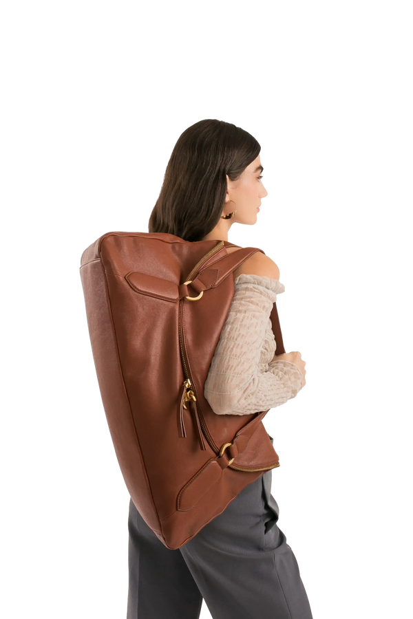 Mochila marrom de couro com detalhes dourados, usada por mulher em look sofisticado e moderno