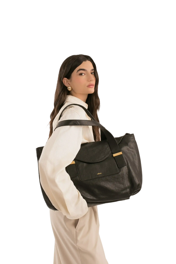 Bolsa preta de couro com alça larga e detalhes dourados, usada por mulher em look sofisticado