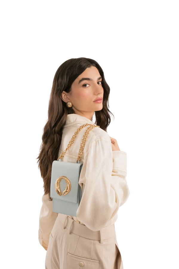 Bolsa azul clara com corrente dourada e detalhe metálico, modelo sofisticado para look elegante