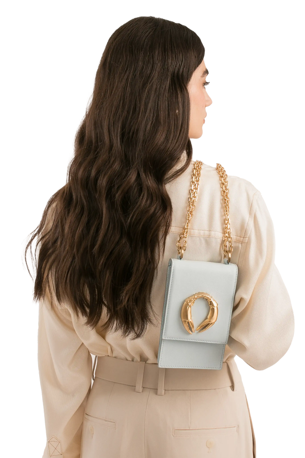 Bolsa mini azul clara com detalhe dourado e corrente, usada por mulher com look sofisticado