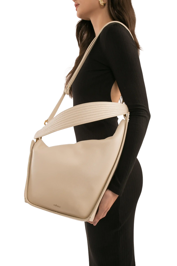 Bolsa bege com alça larga e design moderno, usada por mulher em look preto. Bolsa sofisticada e funcional.