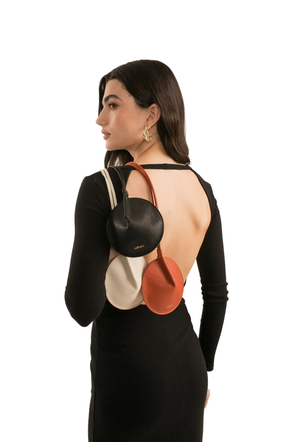 Bolsa redonda preta, branca e laranja com alça transversal, modelo Esthera, usada por mulher de vestido preto