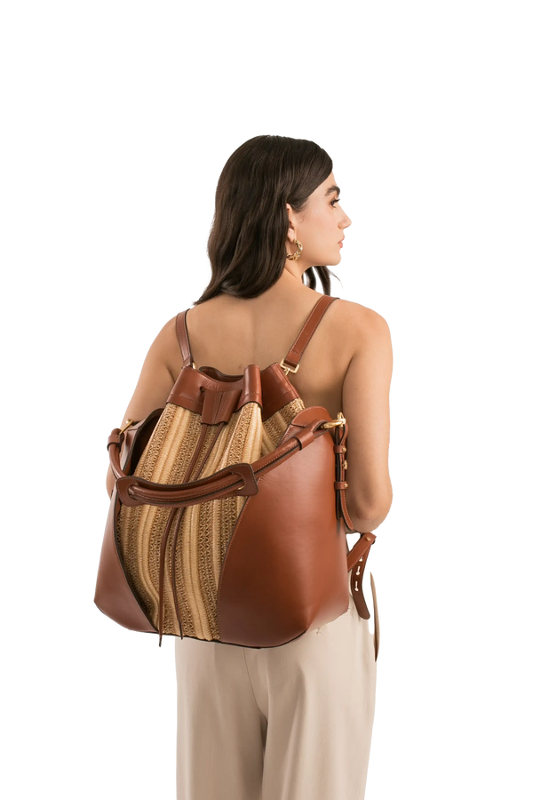 Bolsa bucket em couro marrom e palha, com alças e detalhes em metal dourado, usada por modelo de costas.