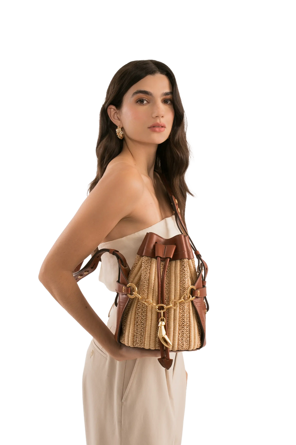 Bolsa de palha com detalhes em couro marrom e corrente dourada, modelo bucket bag para uso diário e sofisticado.