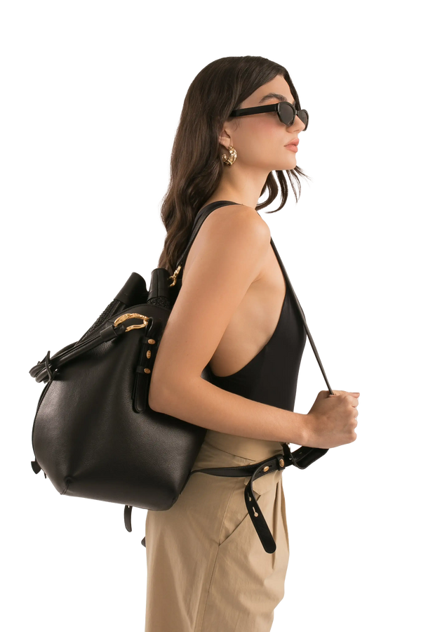 Bolsa preta de couro com alça longa e detalhes dourados, usada por modelo com óculos escuros e look sofisticado.