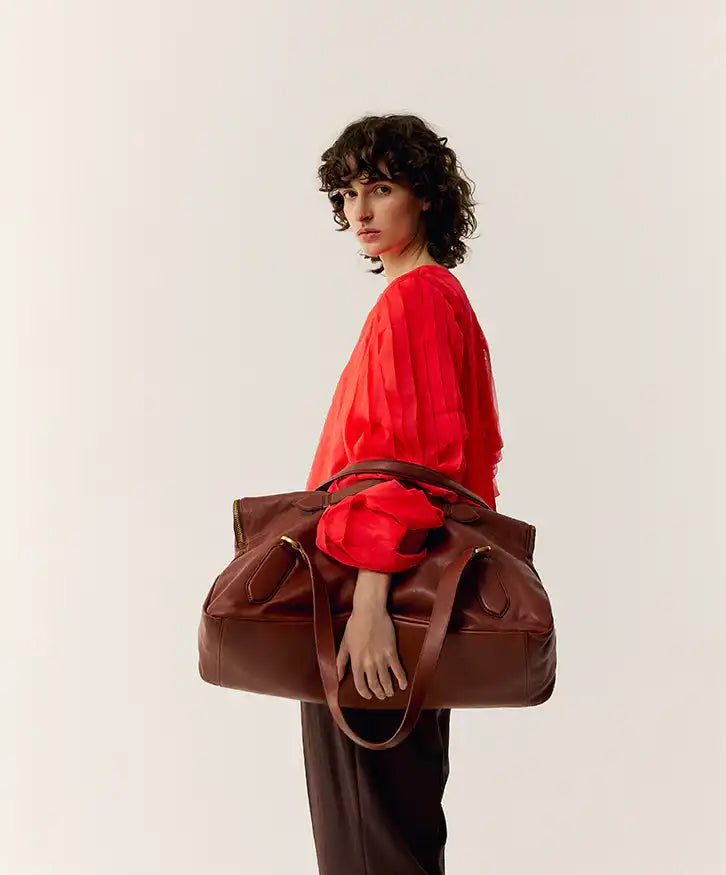 Bolsa marrom de couro com alça, usada por mulher em blusa vermelha, estilo sofisticado e funcional