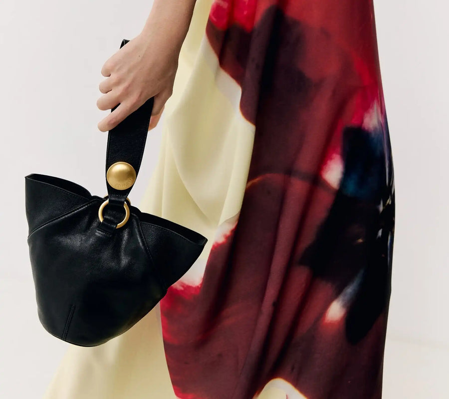 Bolsa preta elegante com detalhes dourados, combinando com vestido estampado